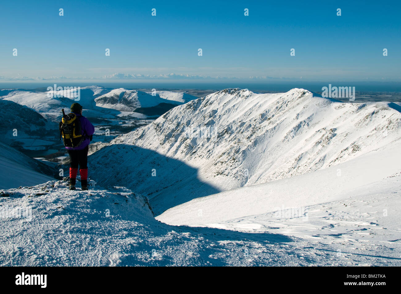 A walker on Sand Hill (Hopegill Head) in winter with Gasgale Crags behind, Grasmoor Fells, Lake District, Cumbria, England, UK Stock Photo