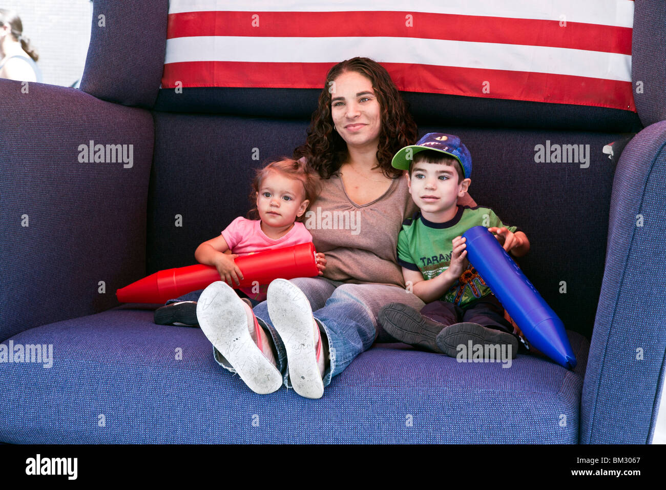 proud patriotic mom poses in oversize club chair with small son & toddler  daughter at Ninth Avenue International Food festival Stock Photo - Alamy