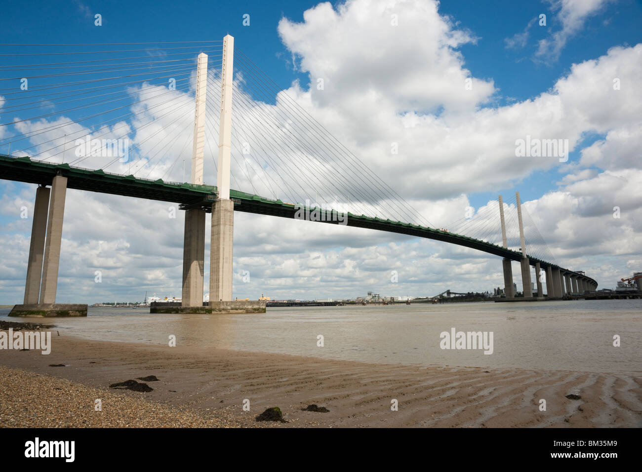 Queen Elisabeth II bridge over river Thames in Dartford with pebbles in the foreground against blue sky with white clouds Stock Photo