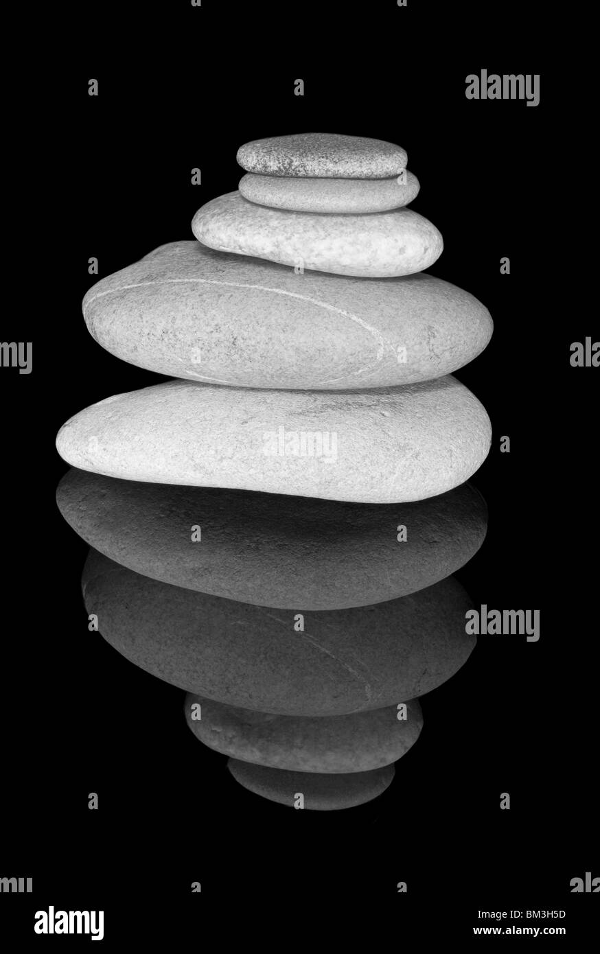 Still Life of a Stack of Beach Pebbles on a Black Background and Reflective Glass. Stock Photo