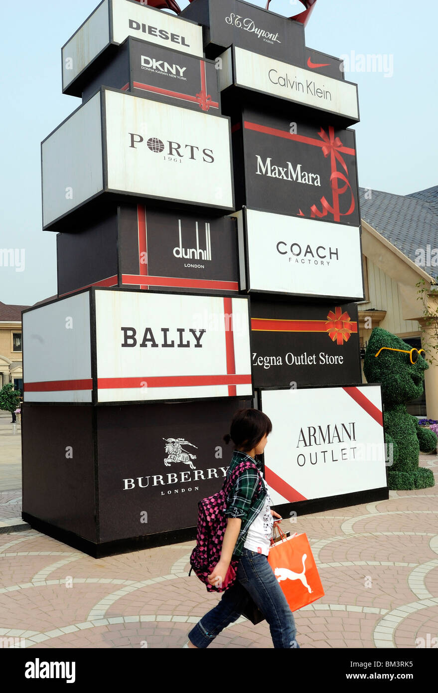 Chinese lady carrying shopping bag past luxury brands bill boards at Beijing Scitech Premium Outlet Mall Beijing, China. 2010 Stock Photo