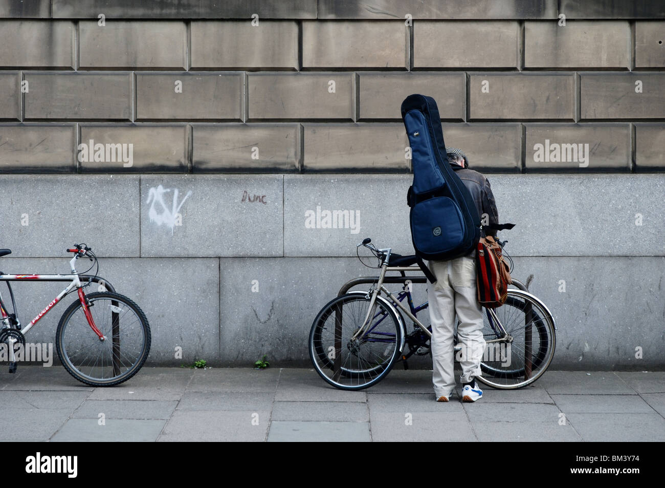 A cyclist with a guitar on his back chaining his bicycle to a rail in