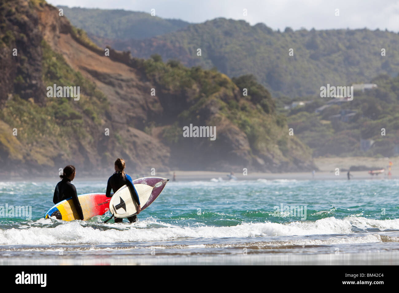 Young surfers head into the waves. Piha, Waitakere Ranges Regional Park, Auckland, North Island, New Zealand Stock Photo