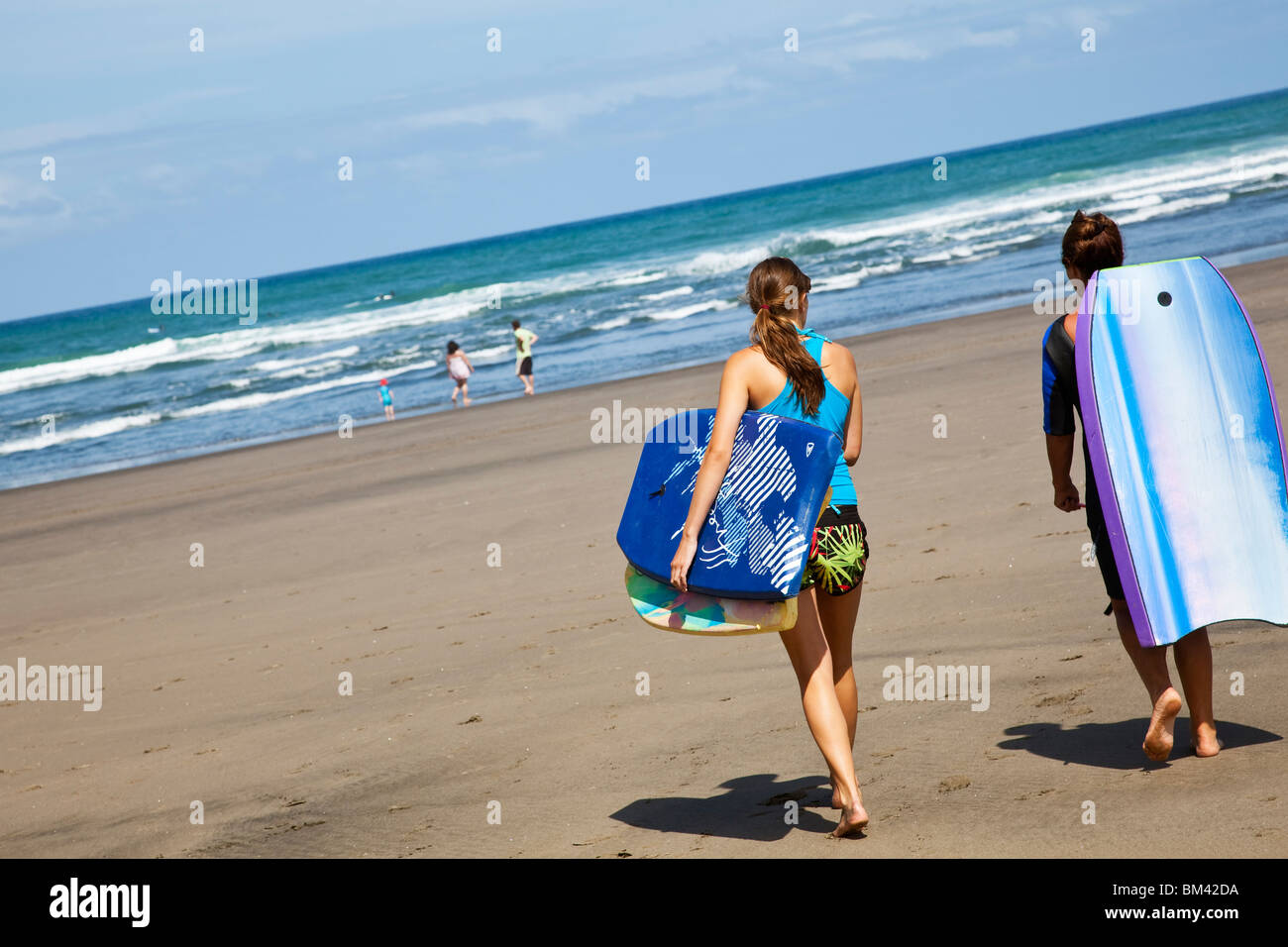 Swimmers carry boogie boards down to the beach. Piha, Waitakere Ranges