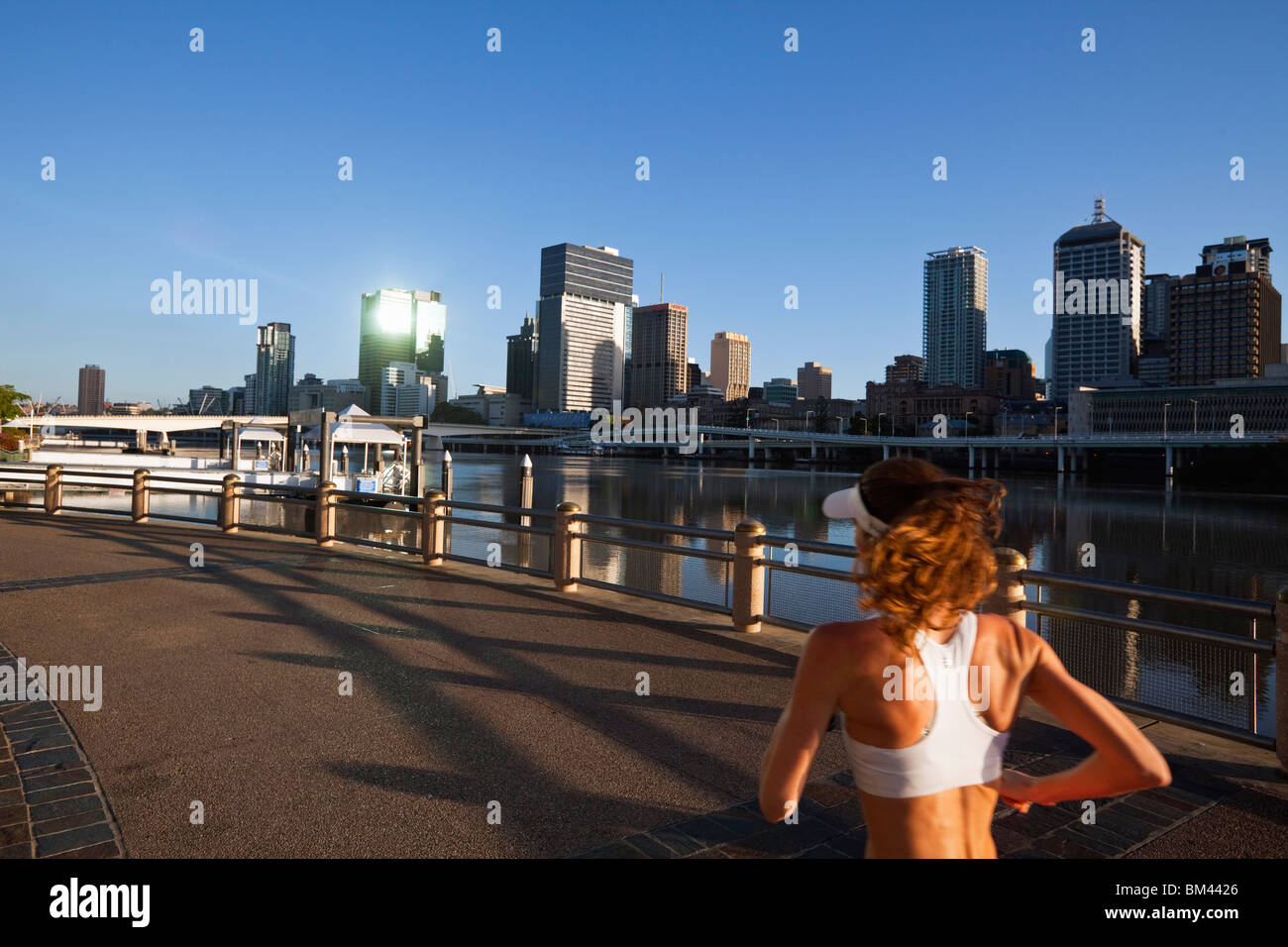 Jogger on the riverside at South Bank with city skyline in the background. Brisbane, Queensland, Australia Stock Photo