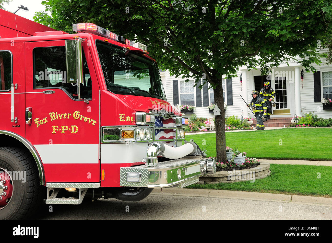 Firemen walking out of front door of a house during response to a suburban fire call Stock Photo