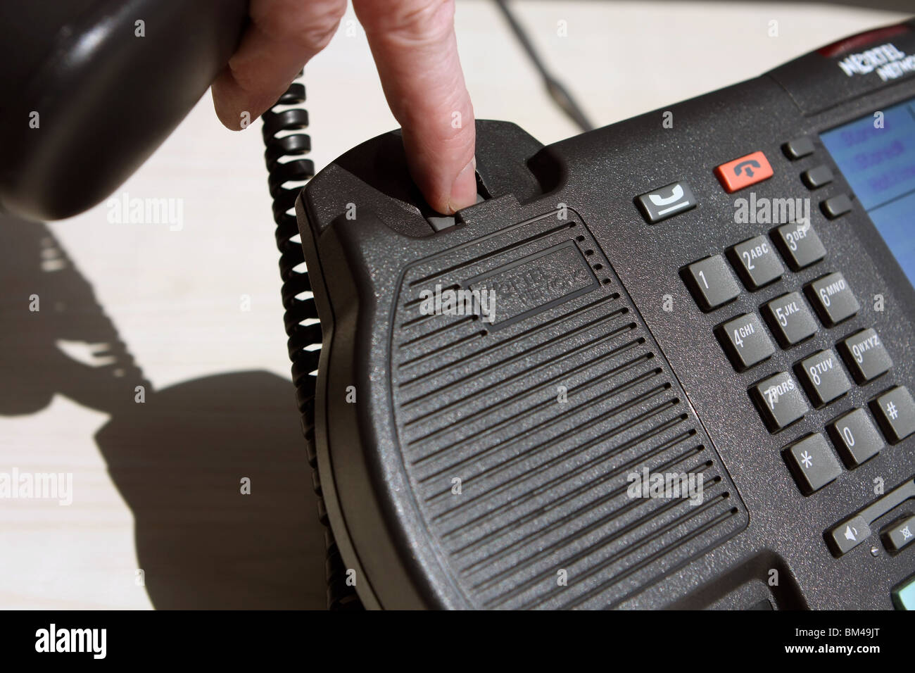 part of a telephone with the receiver off the hook and a finger