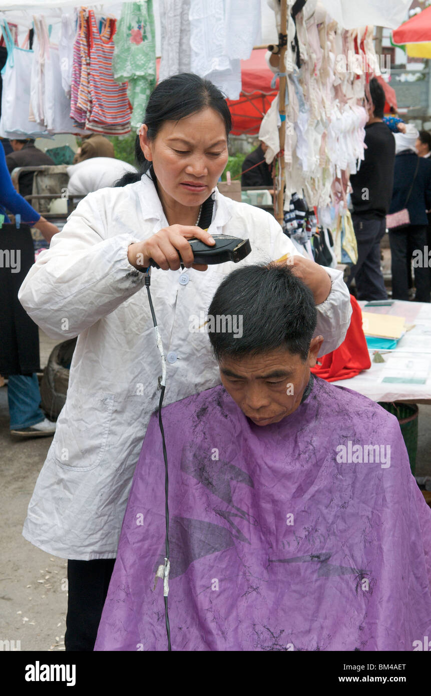 Female barber cutting clients hair in street market Kaili Guizhou Province China Stock Photo