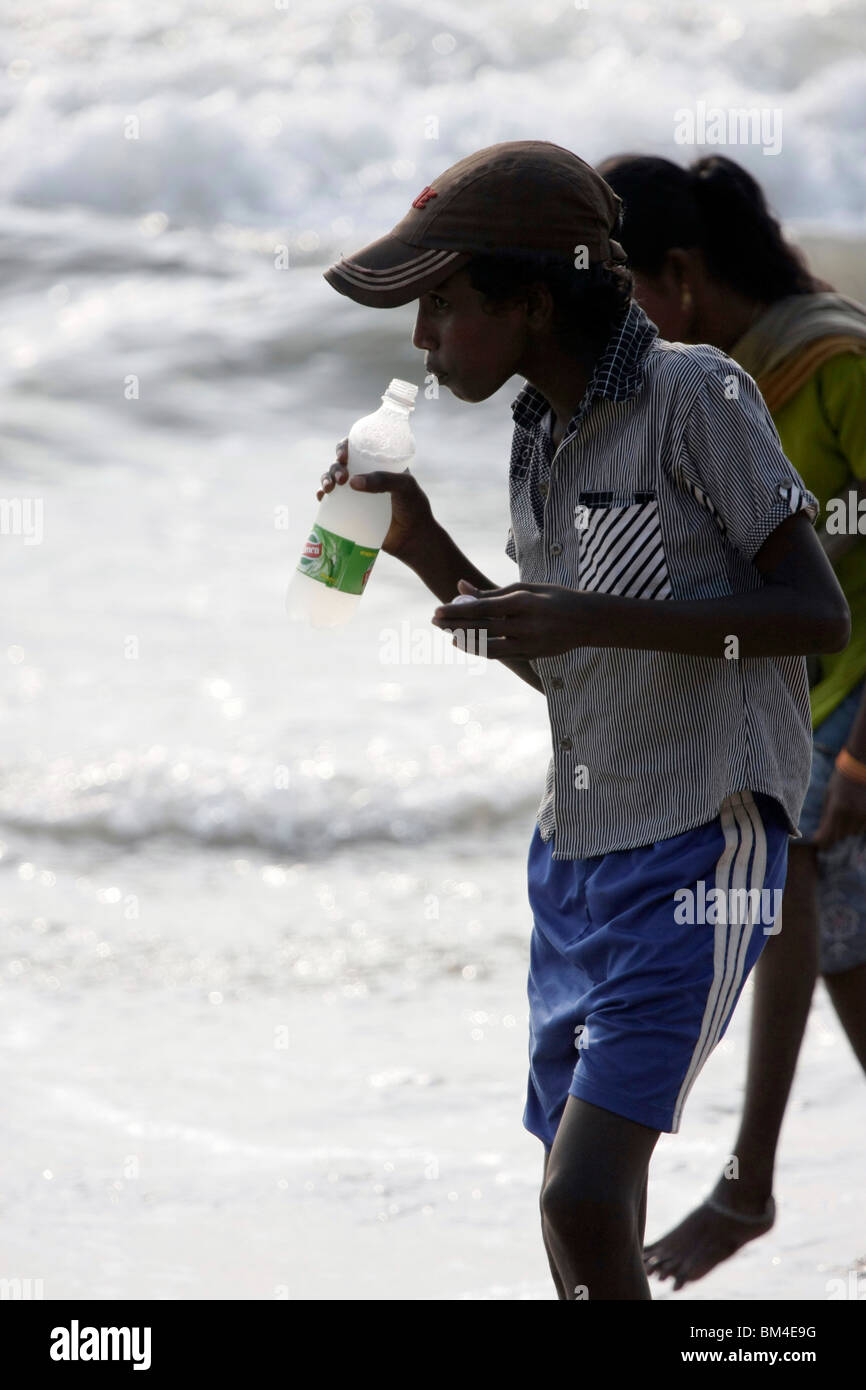 thirsty indian boy drinking soft drinks from a plastic bottle in beach