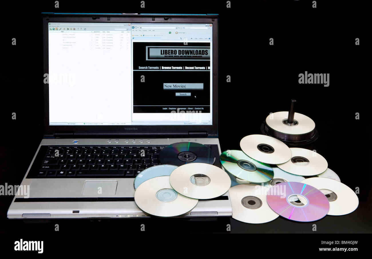 Illegal download website and bittorrent  site on a computer next to a pile of copied DVDs. Stock Photo