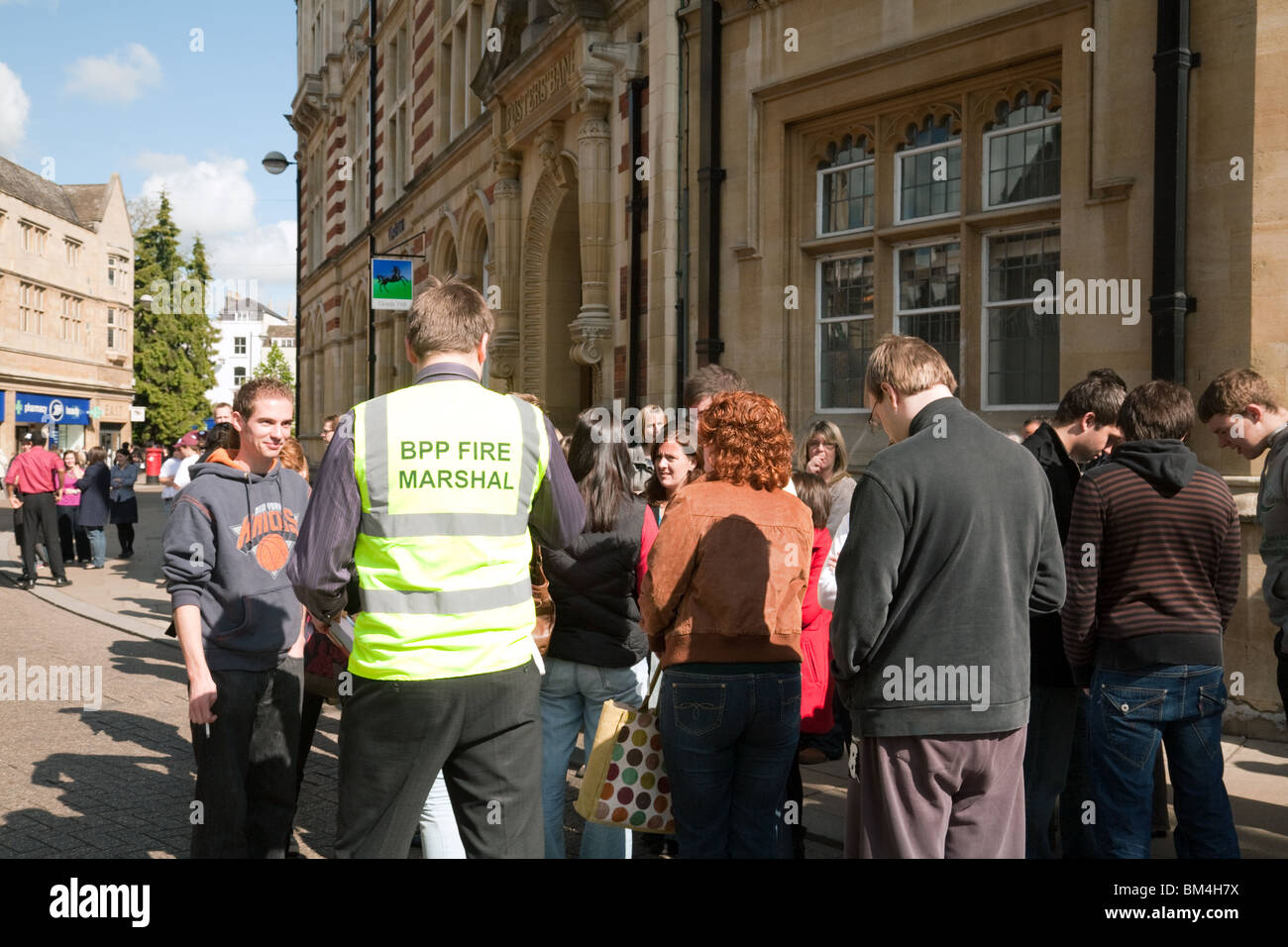 Staff and customers waiting outside Lloyds Bank with a BPP Fire Marshal, Cambridge during a fire alarm drill, Cambridge UK Stock Photo