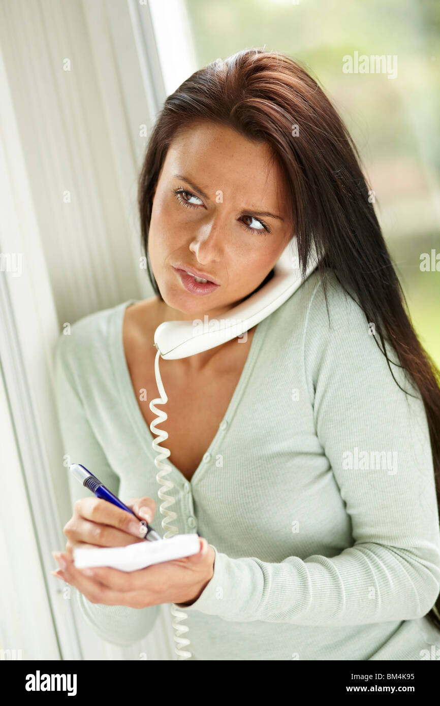 Woman writing notes whilst on phone Stock Photo