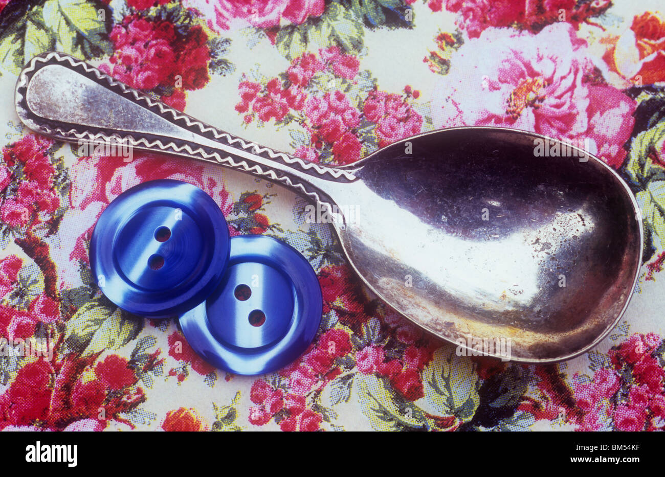 Close up of old silver tea caddy spoon with two blue buttons on pink