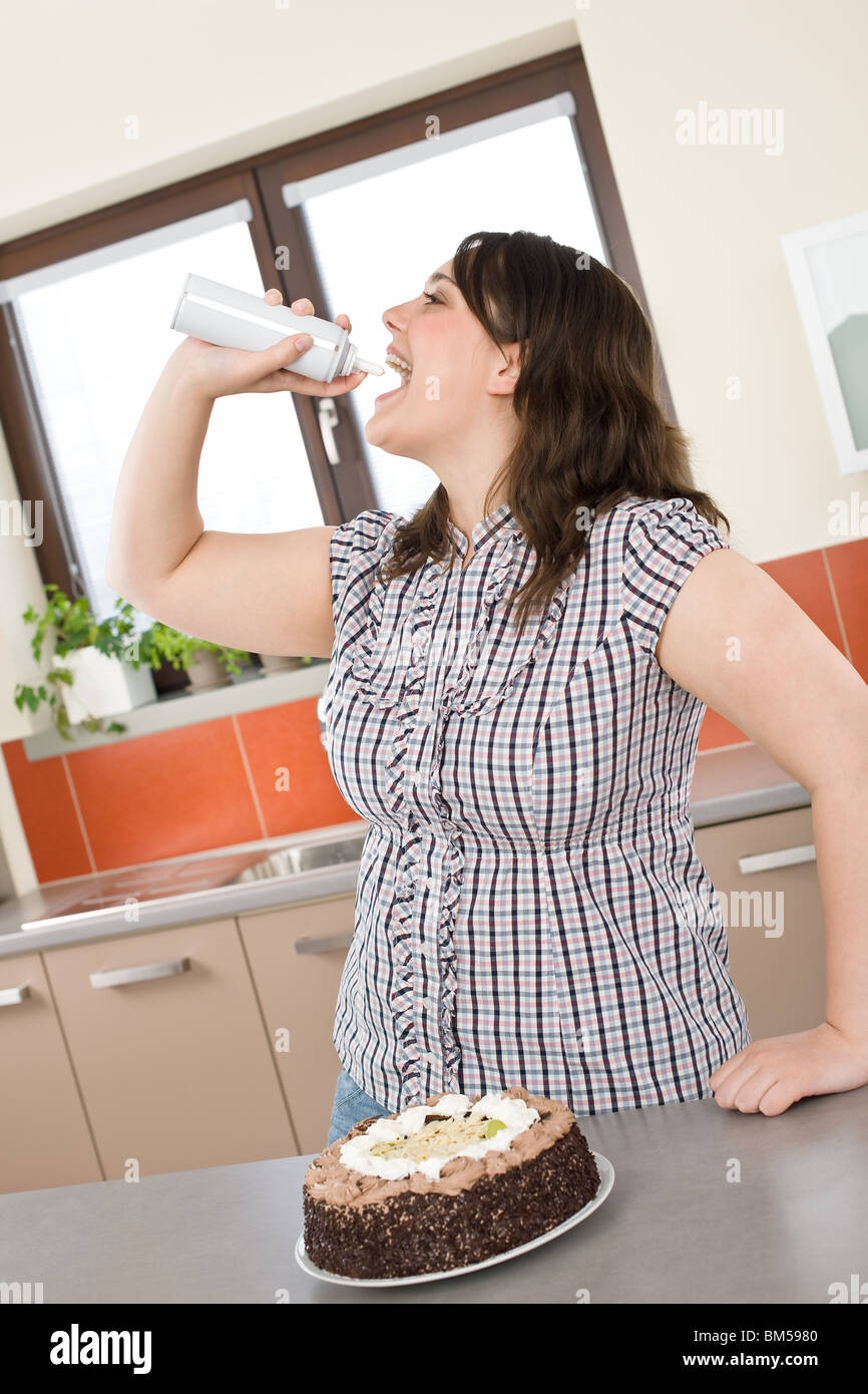 Plus size woman eat whipped cream in modern kitchen with chocolate cake Stock Photo