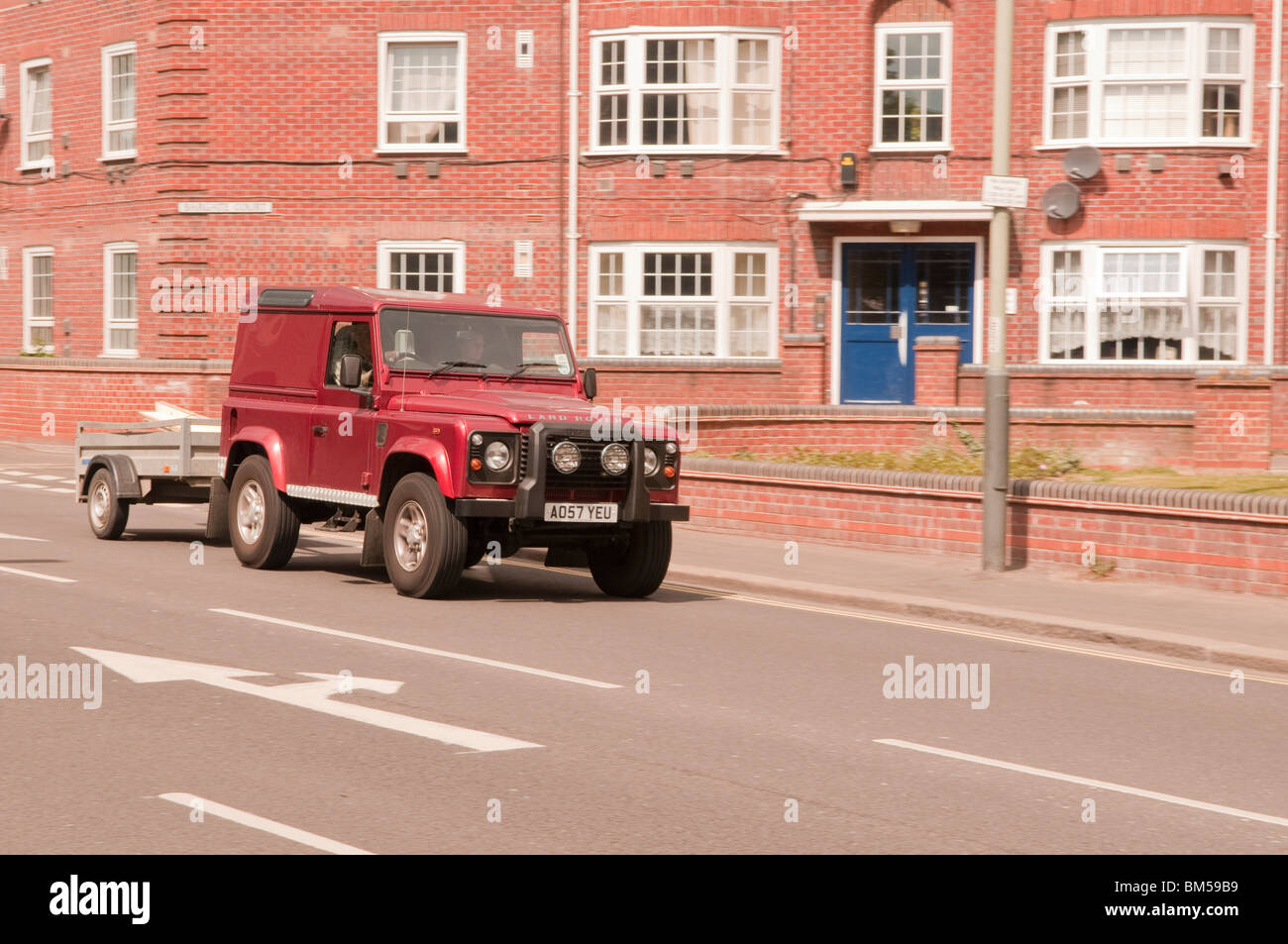 Red Land Rover Defender 90, towing a single axle trailer through Norwich Stock Photo