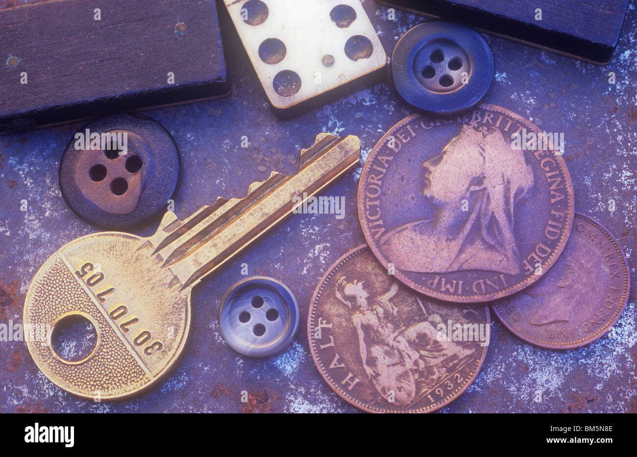 Brass coloured doorkey with domino pieces three male buttons and three old British coins lying on rusting metal tray Stock Photo