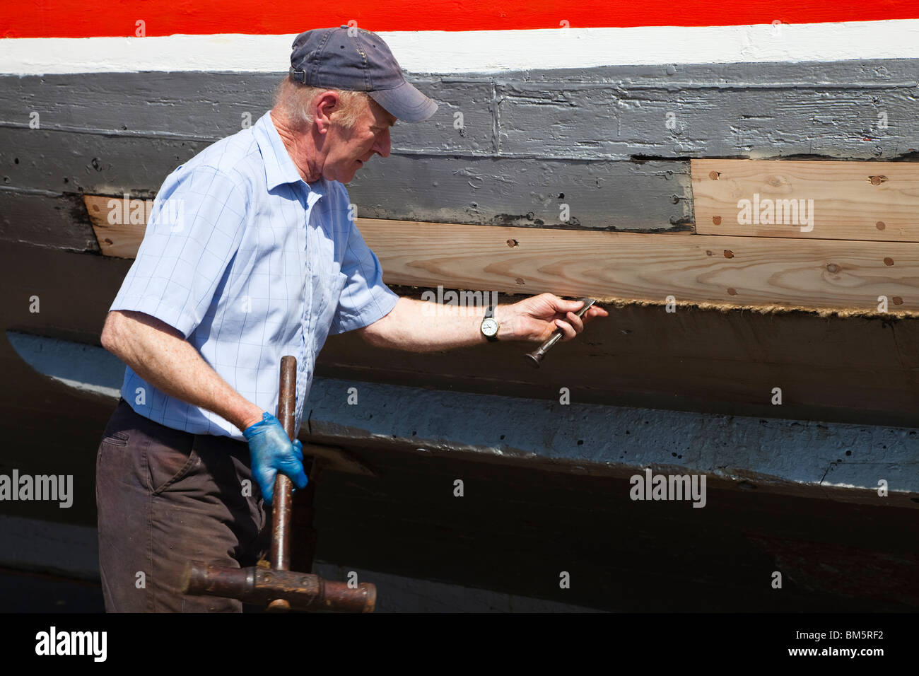 Master craftsmen shipbuilder repairing the wooden hull of a  boat, using a caulking hammer and caulking iron and oakum to seal Stock Photo