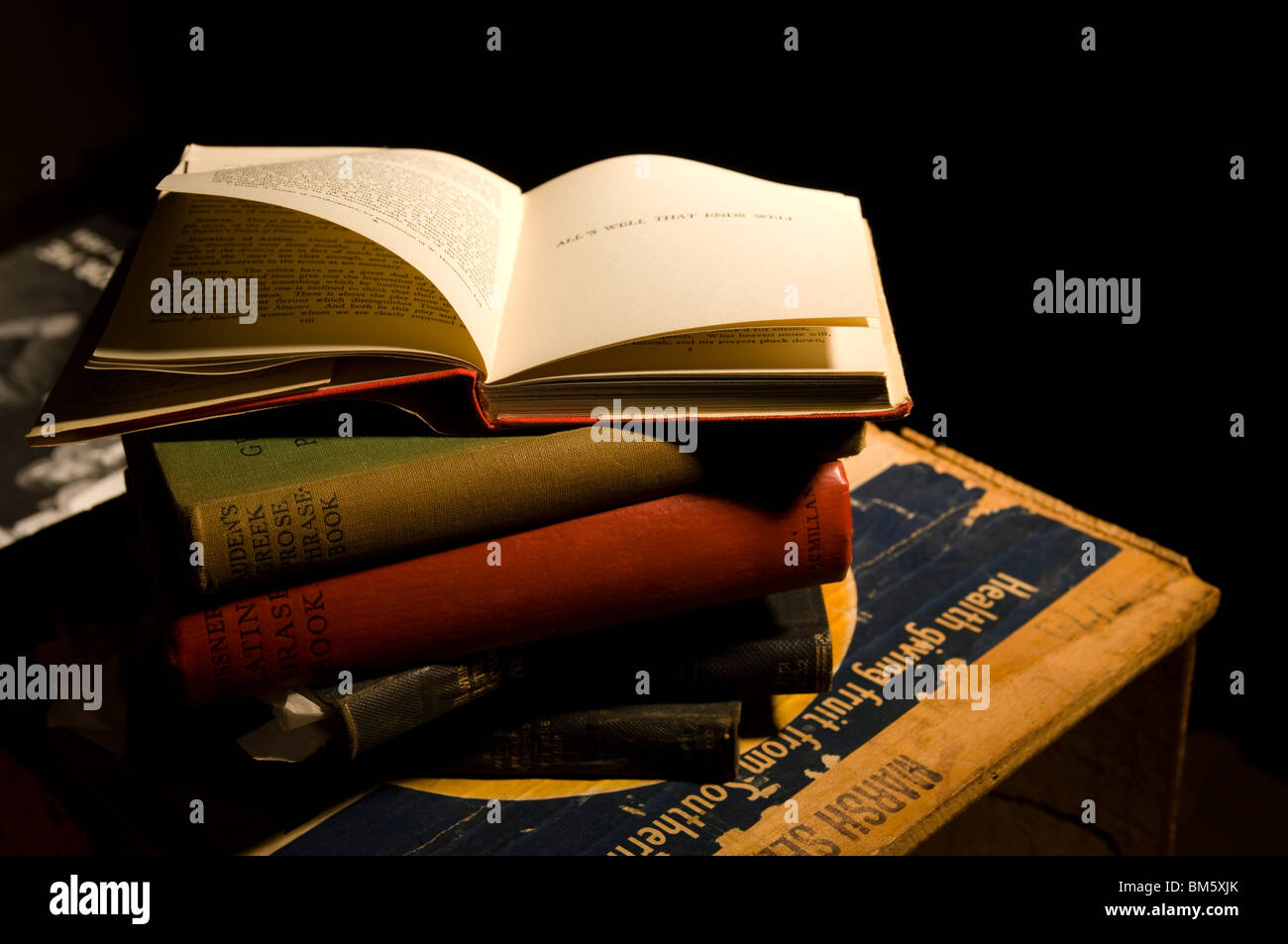 A pile of old books on a crate with top book open to show pages turning Stock Photo