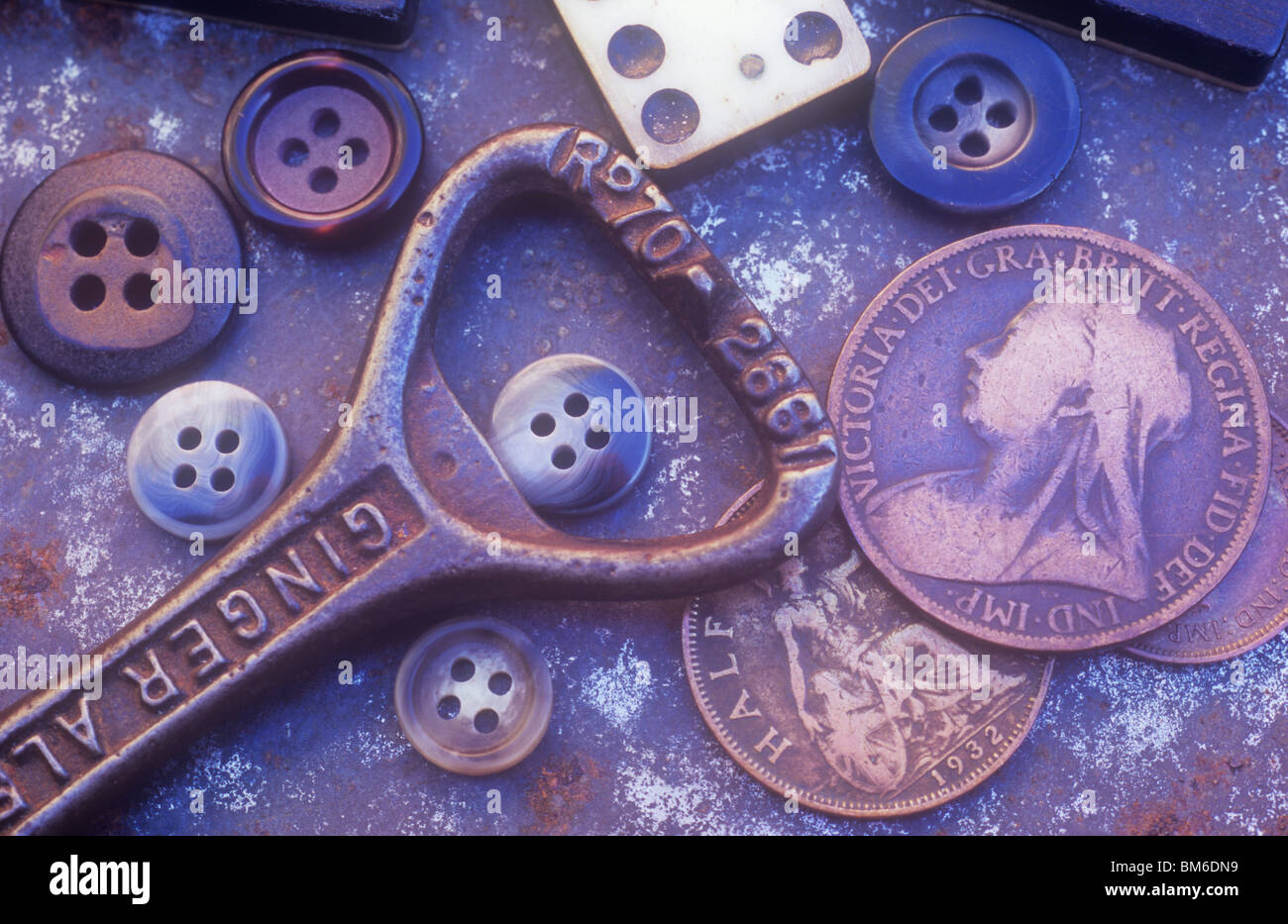 Old bottle opener with domino pieces male buttons and three old British coins lying on rusting metal tray Stock Photo