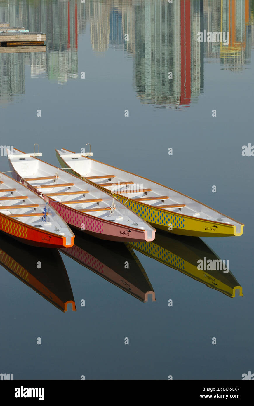 Ten person Dragon Boats sitting empty with reflections of itself and city buildings in the waters of False Creek Vancouver City. Stock Photo