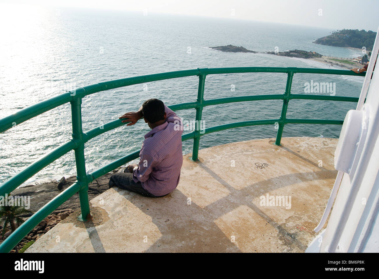 A man sitting dangerously and watching the scenery of Kovalam Beach and cliffs from the top of Light House Stock Photo