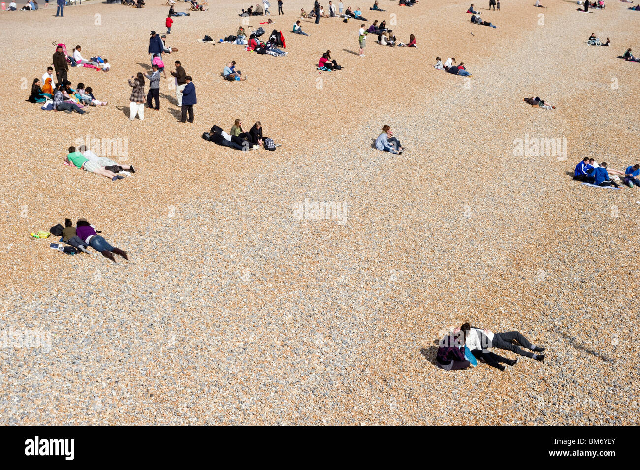 People, tourists, sunbathers and day trippers enjoying fine sunny weather sunbathing on Brighton shingle beach Sussex coast UK Stock Photo