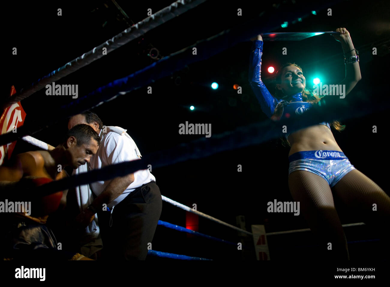 A boxer is attended by his trainer in his ring corner as a woman displays the round change sign during a bout in Mexico City. Stock Photo