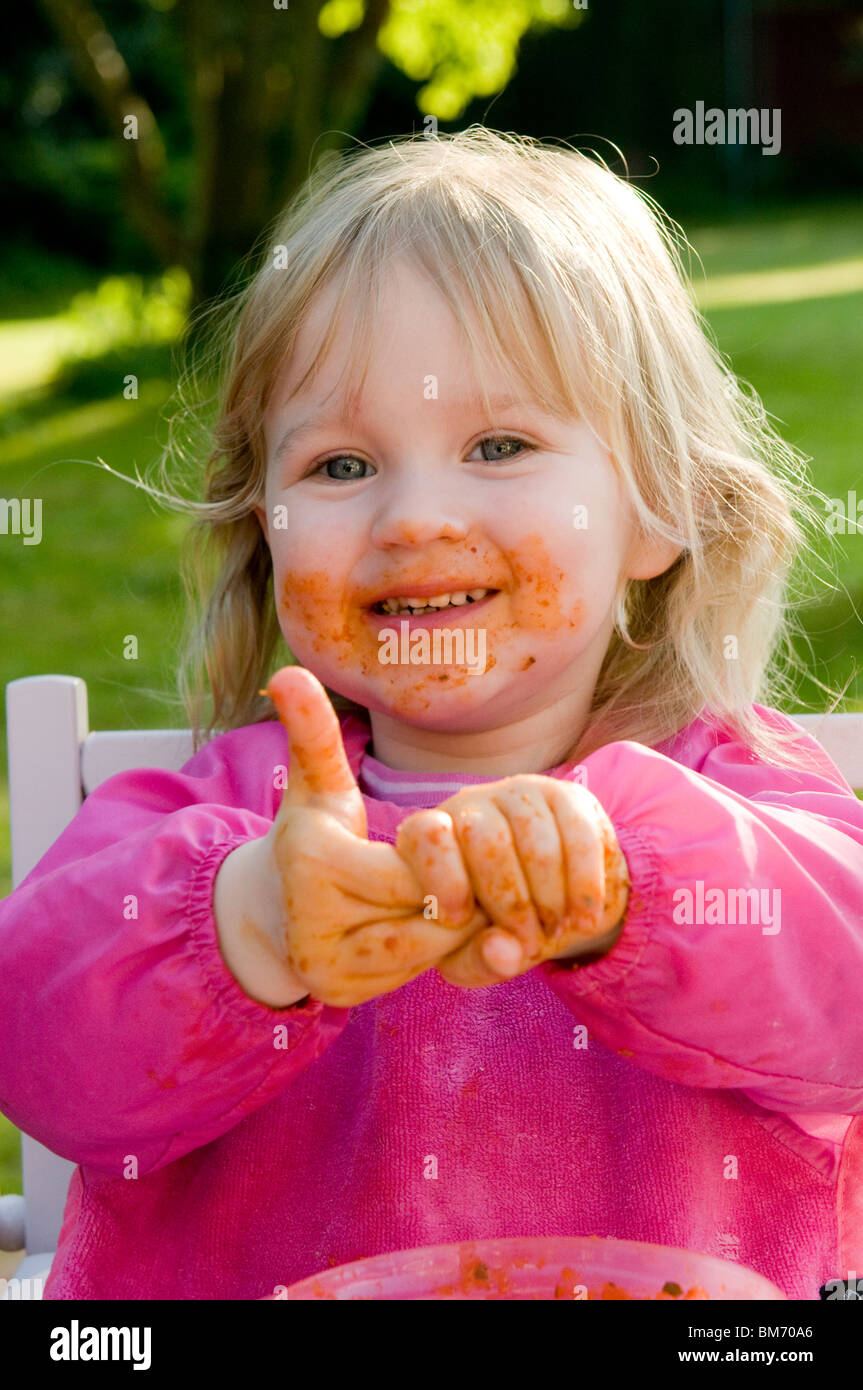 GIRL TODDLER, ENJOYS GETTING MESSY WHILE EATING PASTA IN TOMATO SAUCE Stock Photo Alamy