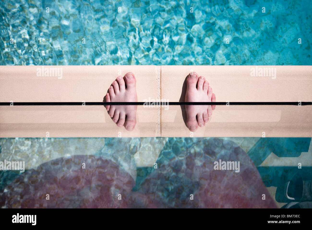 someones feet on the edge of a swimming pool against glass with a reflection making twin feet Stock Photo