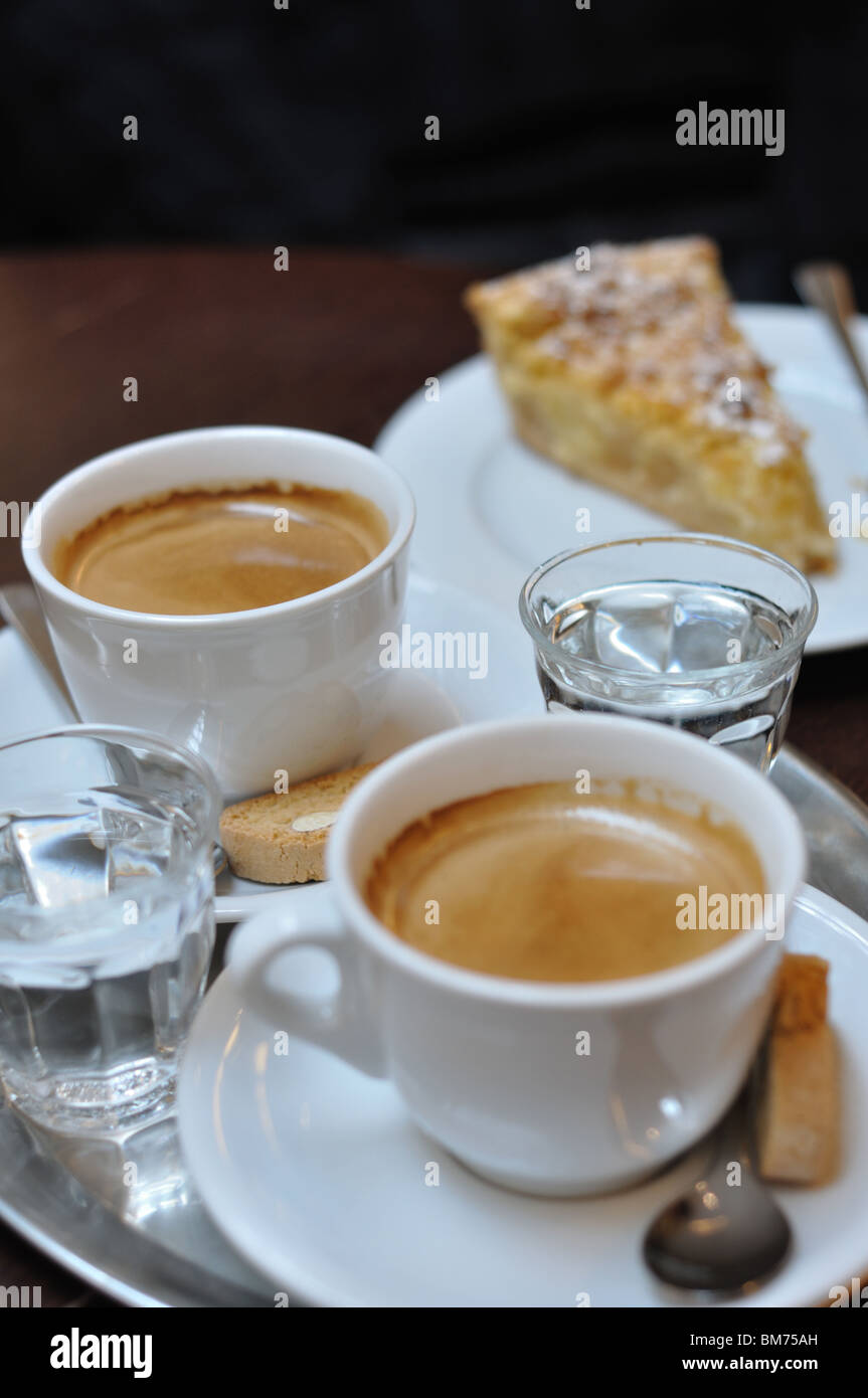 Cups of coffee on a table in a bar, with a piece of cake and two little  glasses of water Stock Photo - Alamy
