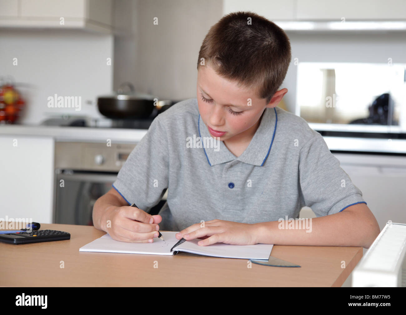 Young boy doing homework on kitchen table Stock Photo