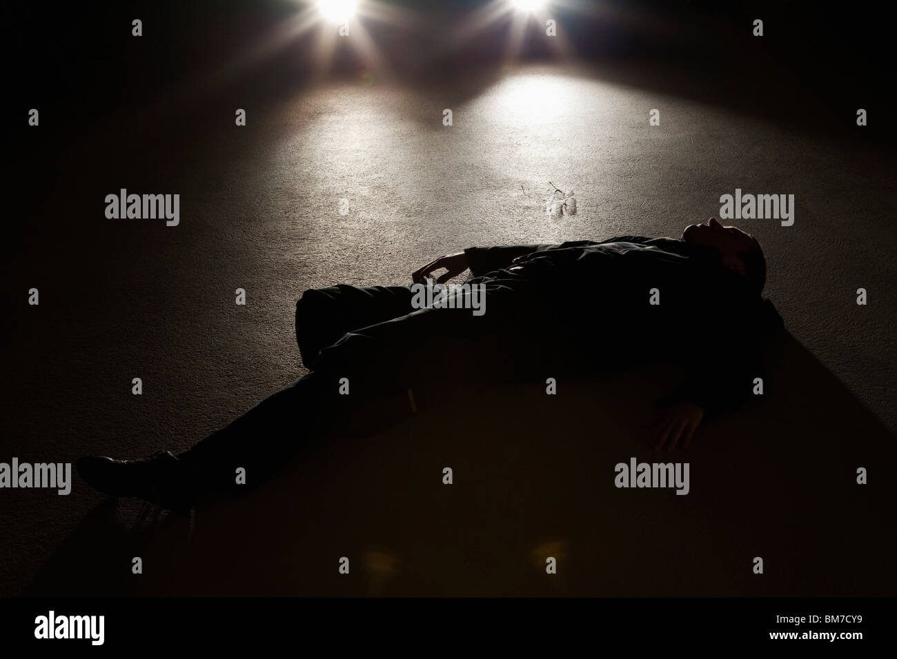 A man lying on the ground in front of a car at night Stock Photo