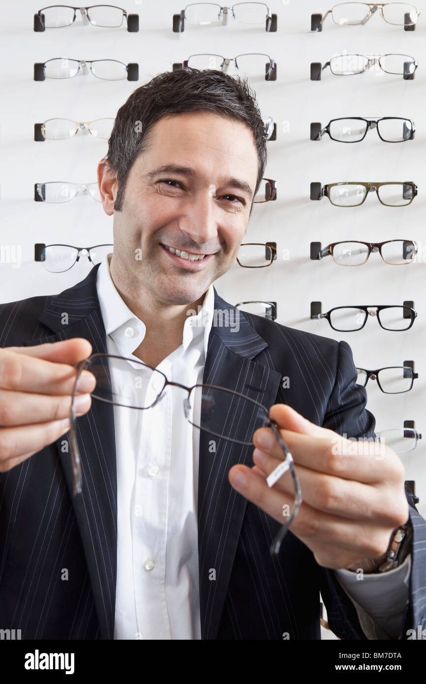 A smiling optician holding up a pair of glasses to the camera in an eyewear store Stock Photo