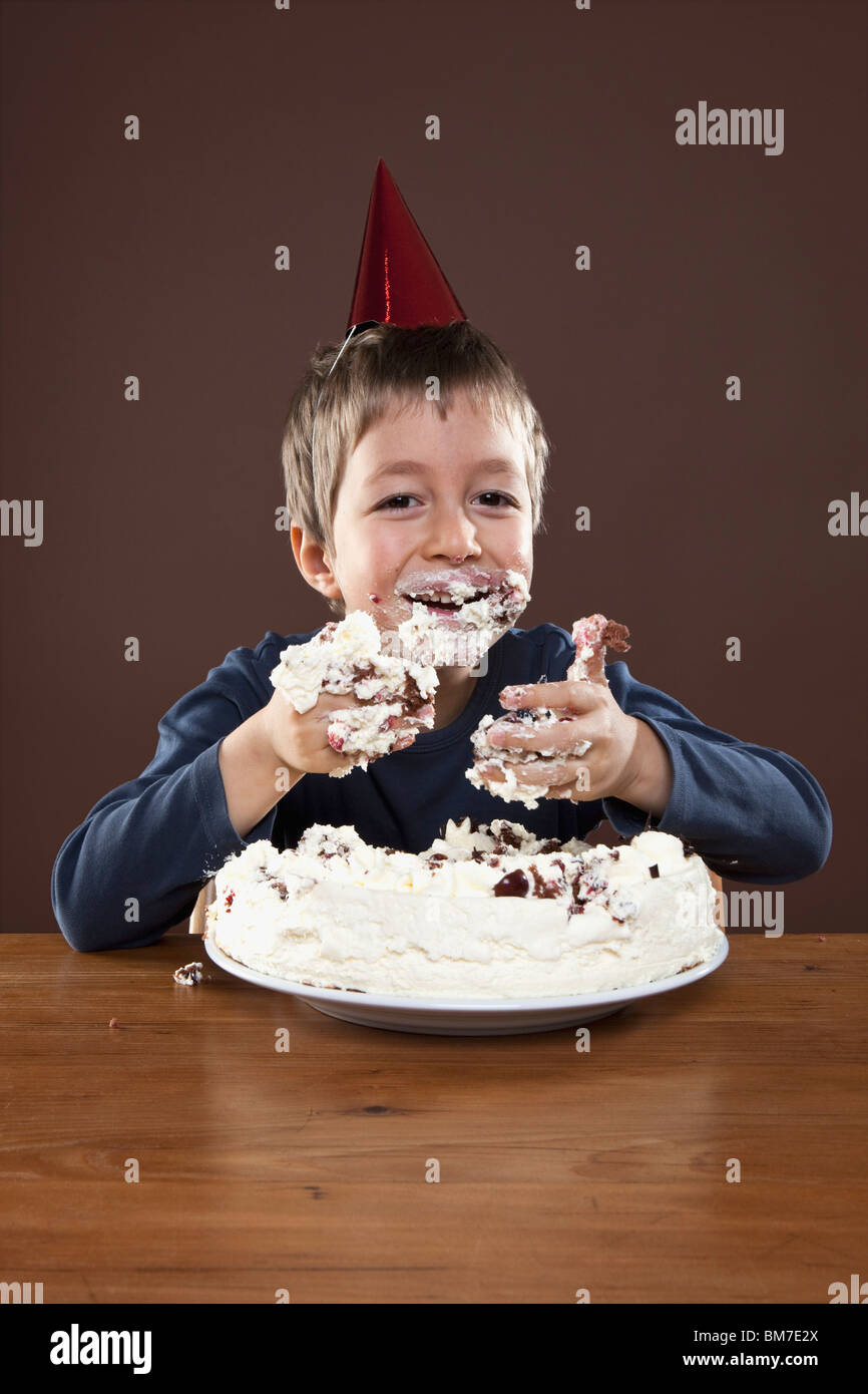 A boy wearing a party hat eating pie with his hands, studio shot Stock