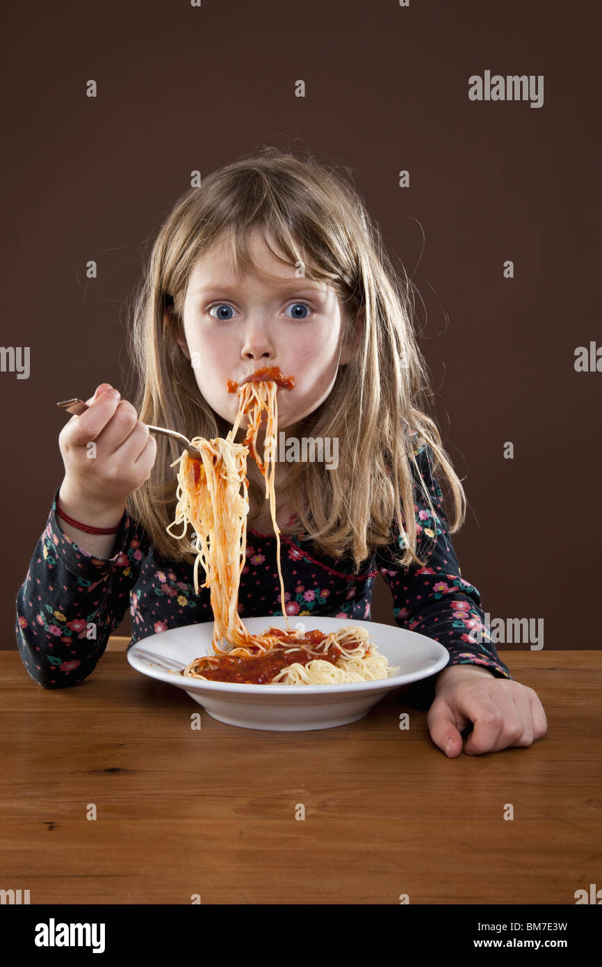 A young girl shoving spaghetti messily into her mouth, studio shot