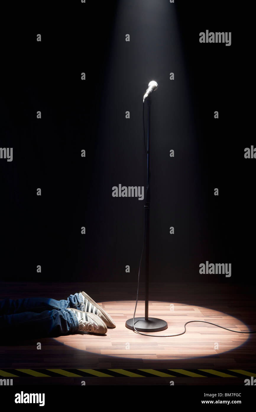 A Person Lying On A Stage Next To A Spot Lit Microphone Stock Photo