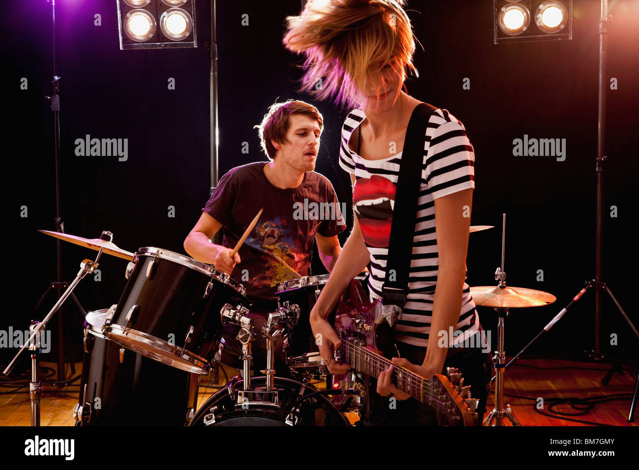 A man playing drums and a woman playing guitar in a rock band performing on stage Stock Photo