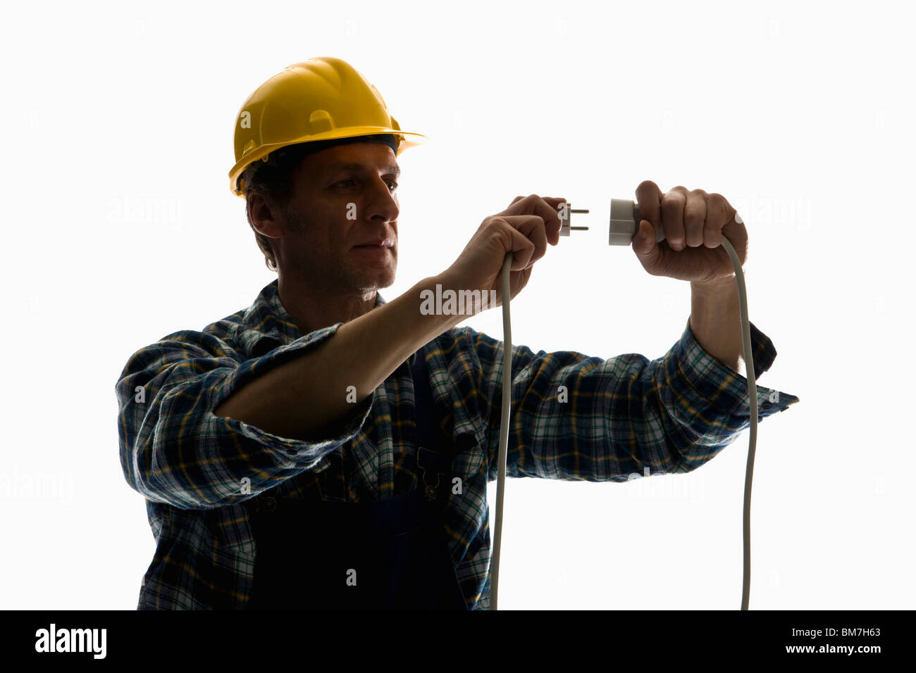A construction worker putting a plug into an extension cord Stock Photo