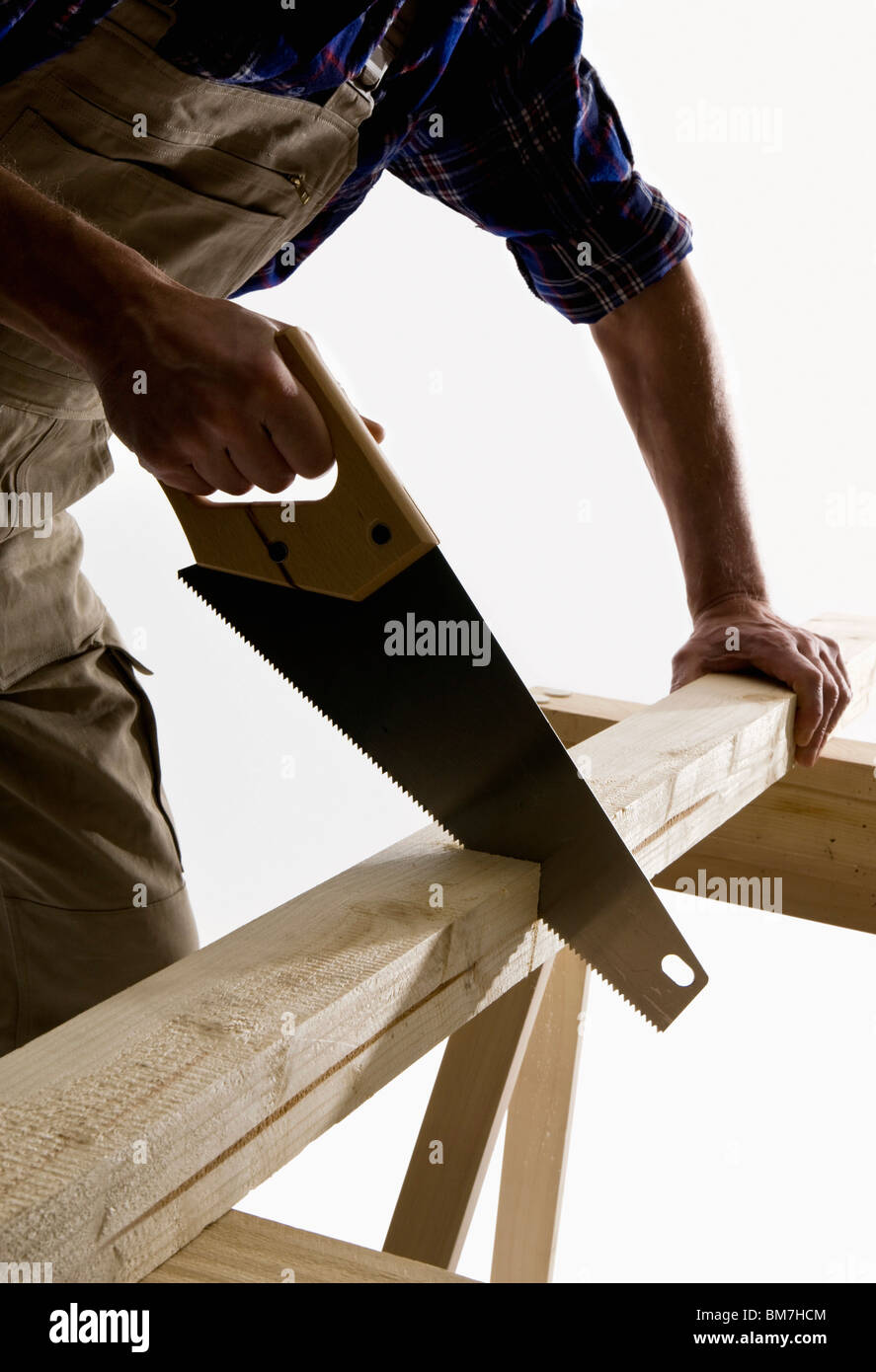 A carpenter sawing a wooden plank, focus on saw Stock Photo