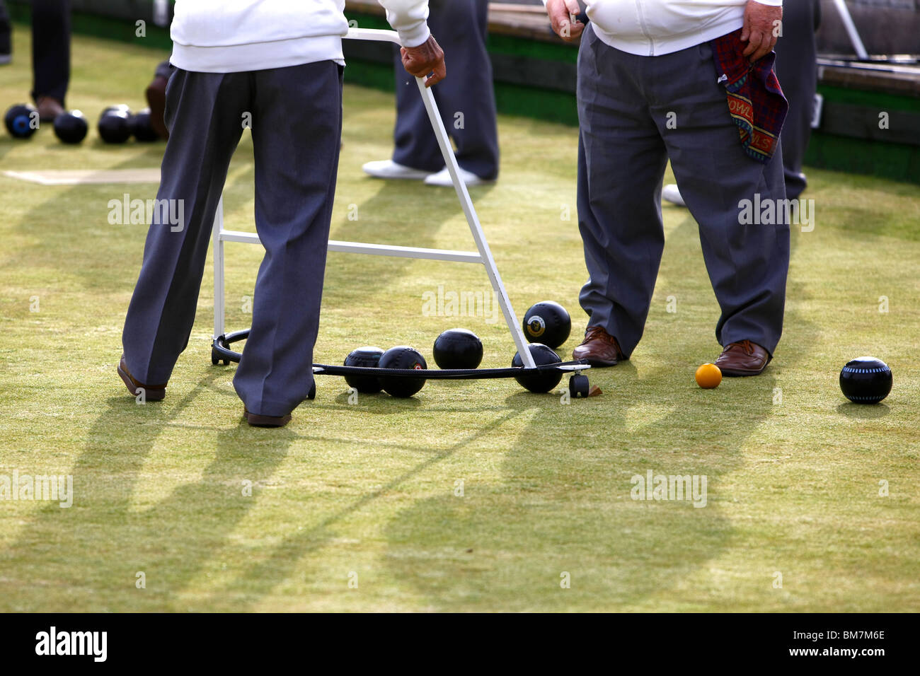 A gentleman player of Crown Green Bowls collects the balls with a customized form of zimmer frame during an evening tournament. Stock Photo