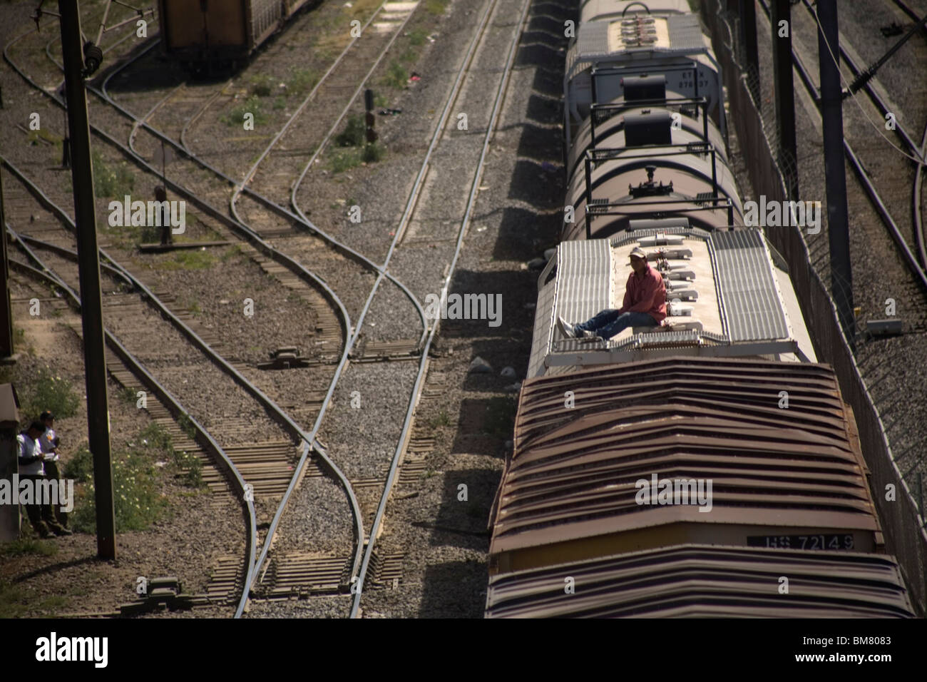 An undocumented Central American migrant traveling across Mexico to work in the US sits on the roof of a train in Mexico City. Stock Photo
