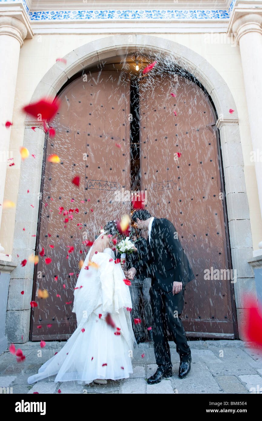 just married couple coming out of the church with people throwing rice and rose petals to them. Stock Photo
