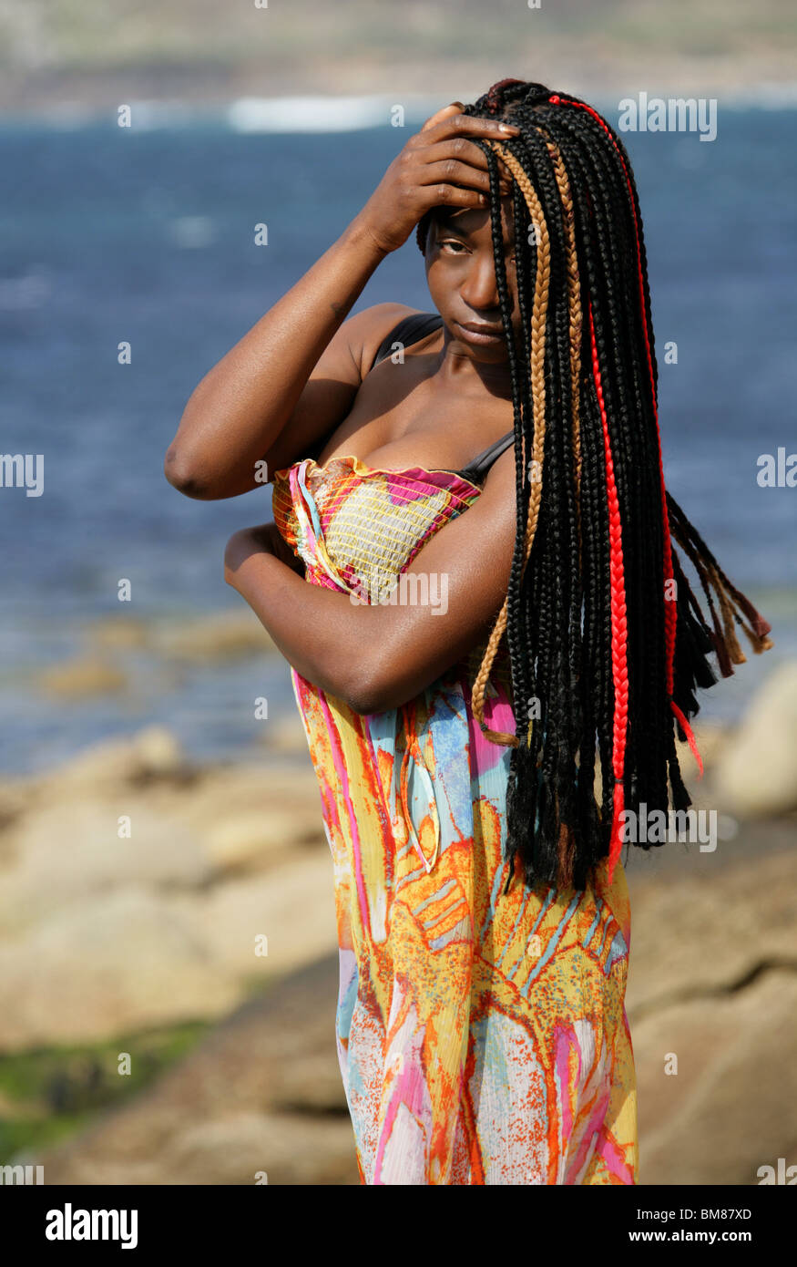 African Woman with Dreadlocks, and Wearing a Colourful Dress, Standing by the Sea. Stock Photo