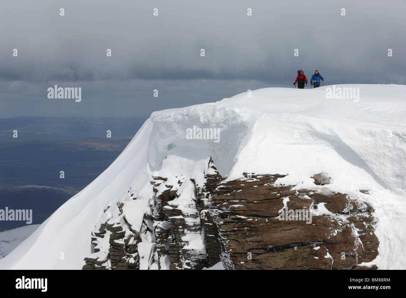 Two mountaineers approaching the summit of Cairn Lochain with a  huge cornice hanging over a cliff. Stock Photo