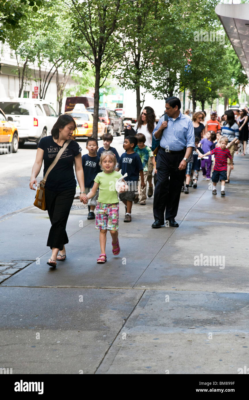boisterous multiethnic group of primary school children walk along Chelsea sidewalk on school outing with teachers Manhattan Stock Photo