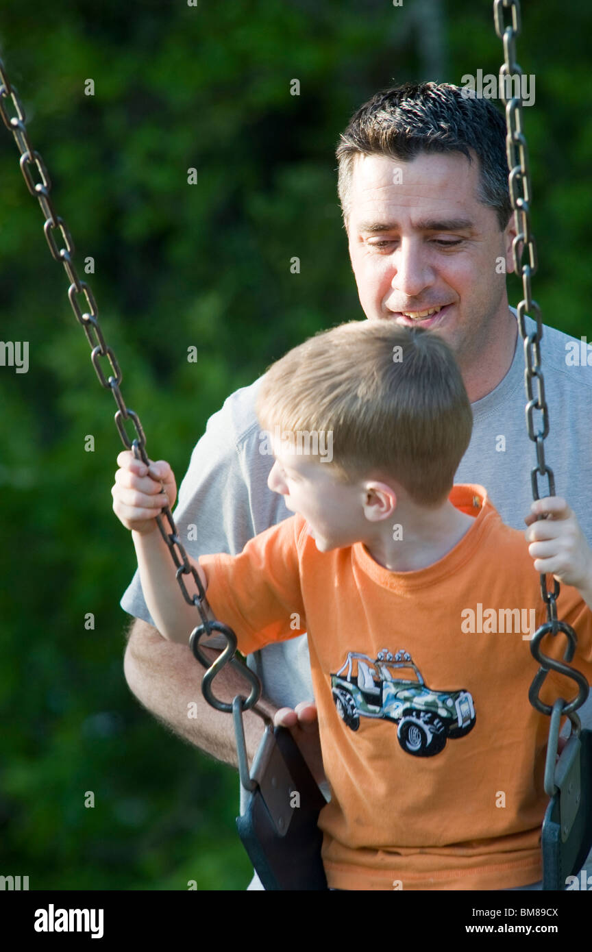 Italian father in his forties pushes his four year old son on a swing. Model Released. Stock Photo