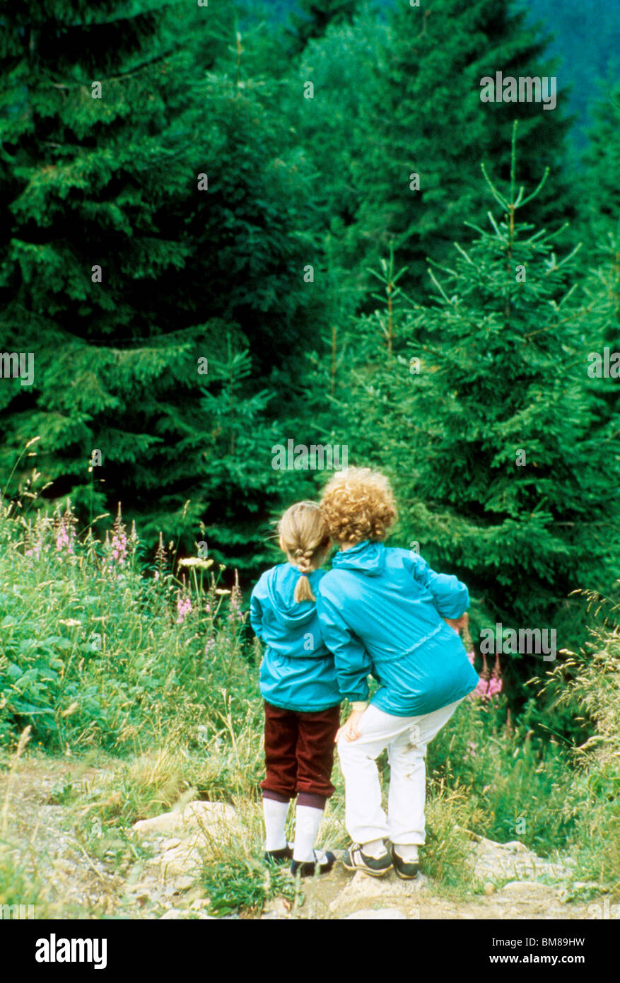 Two sisters ponder entering dark forest in Germany hike trail outdoors fun recreation walk share love afraid fear Stock Photo