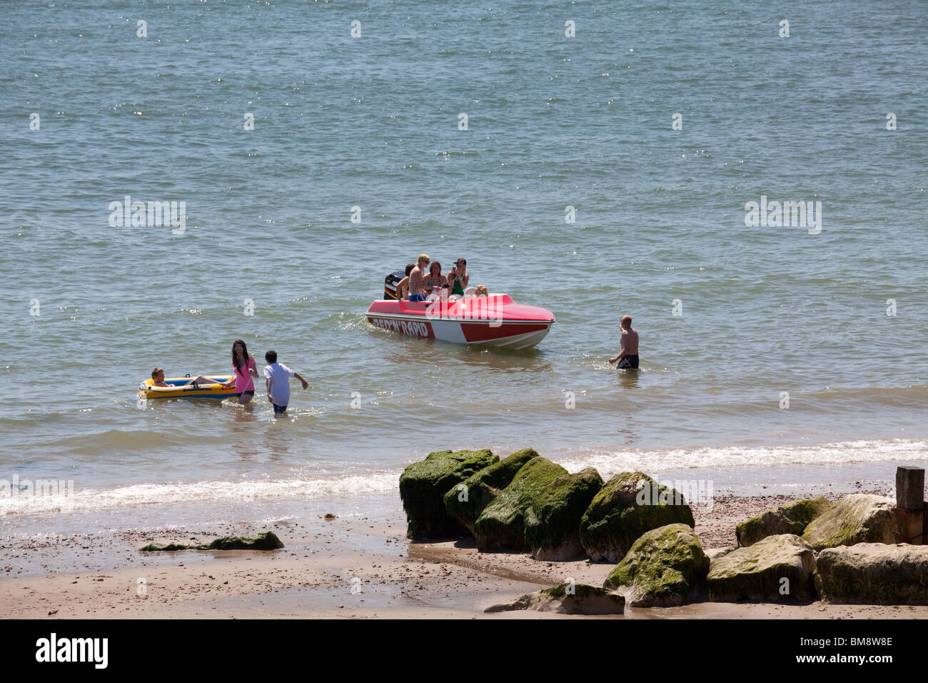 speed boat at beach edge with childs inflatable dinghy and stone groynes Stock Photo