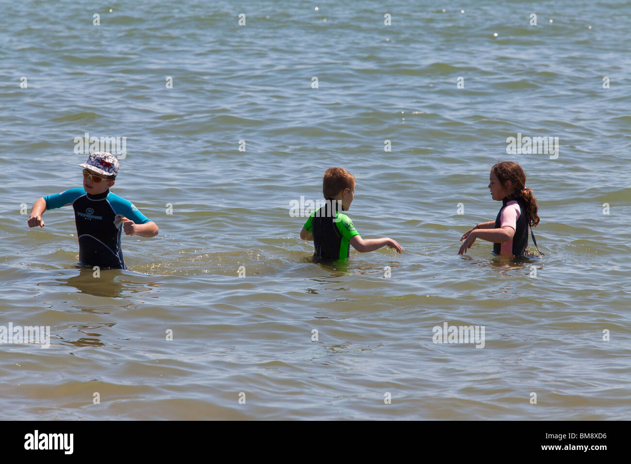 two boys and one girl pre teen in wet suits playing in the sea Stock Photo