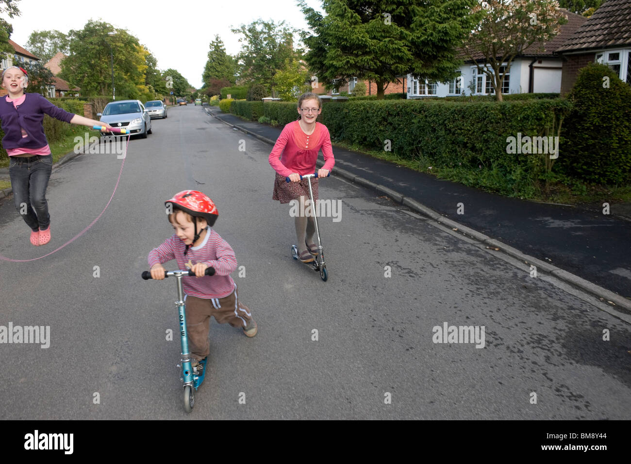 cousins scootering together along a quiet road Stock Photo